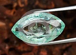 Natural gemstone green emerald in tongs on a brown background