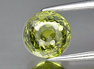 Natural gemstone green garnet grossular in tweezers on a gray background