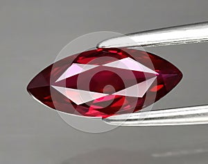 Natural gemstone red ruby in tongs on a gray background