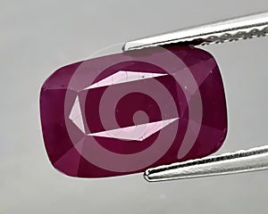 Natural gemstone red ruby in tongs on a gray background