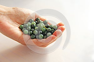 Natural green jade nephrite mineral stones beads. The green jade stone lies in the hands. Hands holding stone on white background