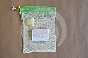 Natural handmade soap on mesh packaging bag and souvenir stone heart on craft paper. Hygiene, body care and health concept.