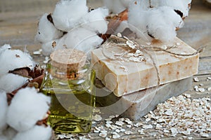 Natural handmade soap, oat flakes, aromatic oil and cotton branch on wooden background.