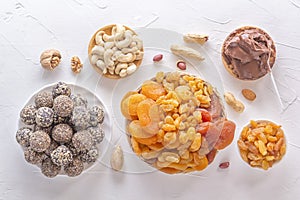 Natural healthy raw energy bites, chocolate paste and mix of dried fruits with nuts on a white table.