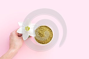 Natural henna powder and white flower in a female hand on a pink background. Concept female beauty and cosmetology. Eyebrow and