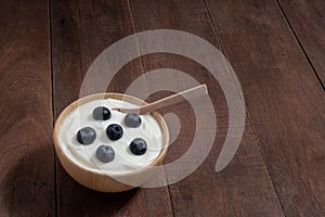 Natural homemade plain organic yogurt mixed with fresh blueberry fruit in white bowl on wood texture background
