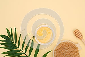 Natural honey in bowl, wooden brush for body massage, honey dipper, green leaf on yellow background with space for text