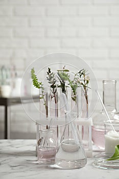 Natural ingredients and laboratory glassware for organic cosmetic product on white marble table