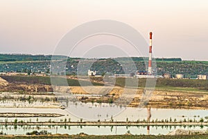 Natural lake is a chalky quarry with a factory smokestack under a green hill on the horizon