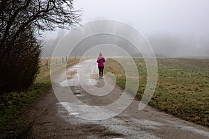 Natural landscape of a foggy morning in the countryside and an athletic woman runs along the road in sportswear.
