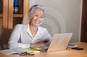 Natural lifestyle office portrait of attractive and happy successful mature Asian woman working at laptop computer desk smiling