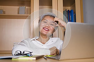 Natural lifestyle office portrait of attractive and happy successful mature Asian woman working at laptop computer desk smiling