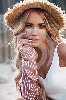 Natural lifestyle portrait of a beautiful gorgeous young woman with long loose blonde hair in a straw hat. Countryside landscape a