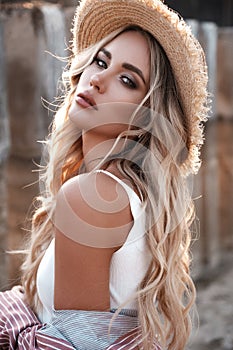 Natural lifestyle portrait of a beautiful sexy young woman with long loose blonde hair in a straw hat. Countryside landscape at th photo