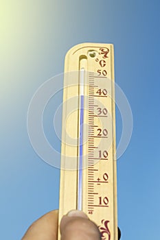 Natural lighting. a human hand holds a wooden thermometer. The temperature on it is very high. Heat