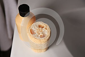 Natural loofah sponge and shower gel bottle on washbasin in bathroom, above view