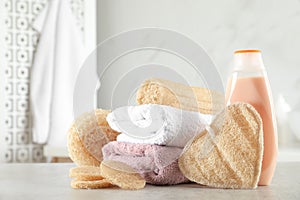 Natural loofah sponges, towels and bottle with cosmetic product on table in bathroom