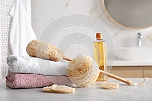 Natural loofah sponges, towels and bottle with cosmetic product on table in bathroom