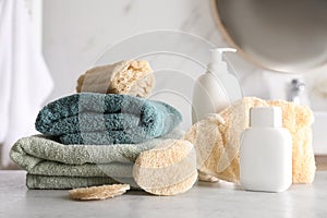 Natural loofah sponges, towels and cosmetic products on table in bathroom