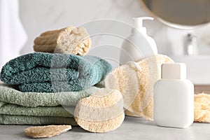 Natural loofah sponges, towels and cosmetic products on table in bathroom