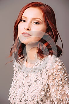 Studio portrait of young beautiful ginger woman in white lace blouse on grey background.