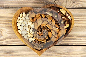 Natural nutritional blend of various nuts in a wooden plate in the shape of a heart symbol on a brown wooden table. A mixture of