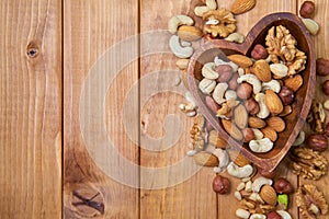 Natural nutritious mix of different nuts in a wooden plate of heart symbol shape on brown wooden table at the right side. Mixture