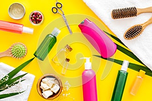Natural oil for hair near scissors, shampoo bottle, and brush on yellow background top view