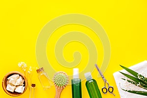 Natural oil for hair near scissors, shampoo bottle, and brush on yellow background top view copyspace