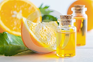 Natural orange essential oil in bottle and cut oranges fruit on white wooden table