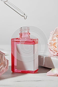 Natural organic beauty oil with rose extract in dropper bottle with blank label on marble background. Skin care concept