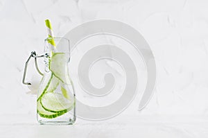 Natural organic cocktail with green cucumber, carbonated water, slices and striped straw in yoke bottle on bright white wood board