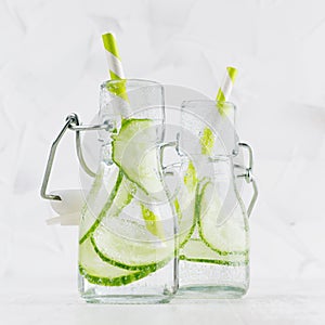 Natural organic cocktails with green cucumber, carbonated water, slices and striped straw in yoke bottles on bright white wood.