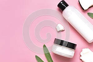Natural organic eco cosmetics with coconut oil. Cosmetic containers with cream and lotion, broken coconut, green leaves on pink
