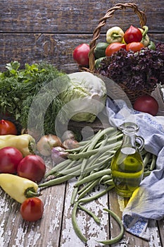 Natural organic fresh vegetables, rich harvest of tomatoes, greenery, olive oil, green beans on a wooden background.