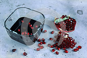 Natural organic pomegranate sause in glass cup, cut pomegranate fruit and pomegranate grains on gray background. Selective focus.