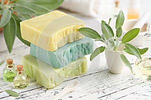 Natural organic soap bars, bottles of essential oil and fresh green sage leaves on white table