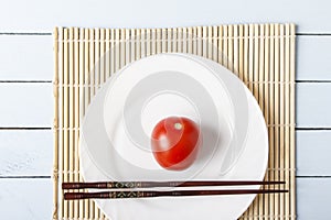 Natural organic tomato and food sticks on white plate. Wooden table with bamboo mat. Chinese and japanese kitchen concept. Top vie