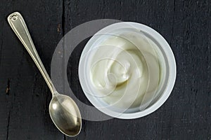 Natural organic white yogurt, Greek yogurt, plastic cup with white yoghurt on black background - overhead photo