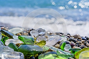 Natural polish textured sea glass and stones on the seashore. Azure clear sea water with waves. Green, blue shiny glass with multi