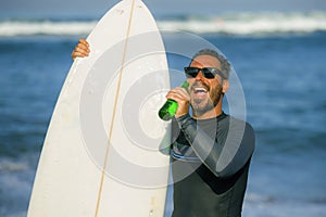 Natural portrait of attractive and happy surfer man on his 40s carrying surf board after surfing morning at beautiful beach in