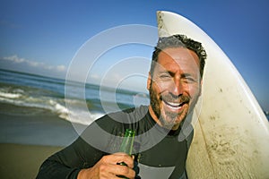 Natural portrait of attractive and happy surfer man on his 40s carrying surf board after surfing morning at beautiful beach in