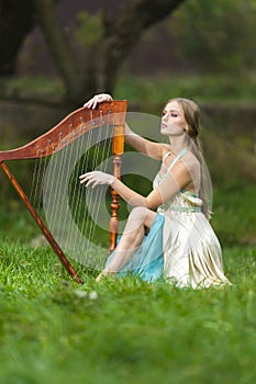 Natural portrait of sensual female harpist woman in light dress playing the harp in park outdoor