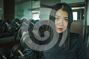 Natural portrait of young beautiful and happy Asian Japanese woman in sport hoodie posing cool at fitness center sitting by