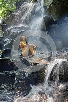 Natural portrait of young beautiful and happy Asian Korean woman in bikini enjoying nature at tropical paradise waterfall with