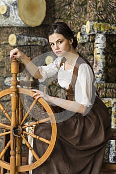 Natural Portrait of Young Brunette Girl Posing With Old Wooden Spinning Wheel in Retro Dress In Village Environment