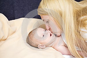 Natural Portrait of Young Caucasian Mother Kissing Her Newborn Baby Boy Lying on Bed