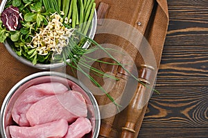 Natural raw ingredients for healthy pet food ingredients in individual bowls on brown wooden background.