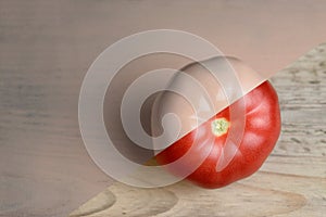 Natural red and beige or ecru half painted tomato on wooden background.