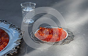 Silver plates with red caviar on gray surface